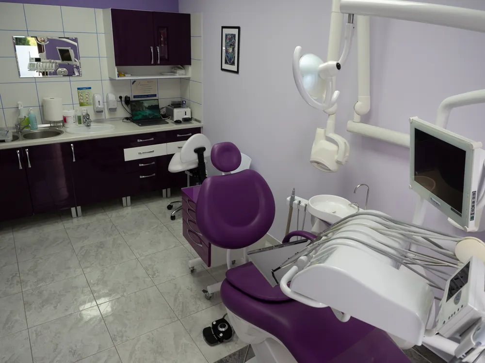 Wnętrze fioletowego gabinetu OL-DENT z lampą zabiegową i sprzętem stomatologicznym